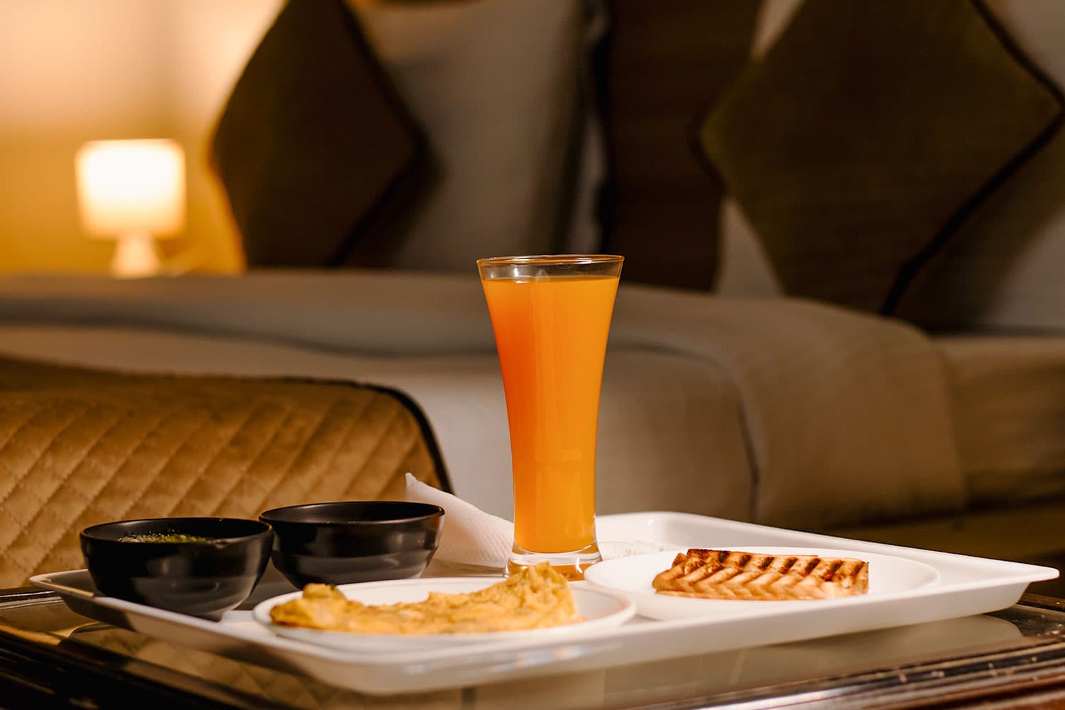 Breakfast tray with orange juice and grilled sandwich beside the bed