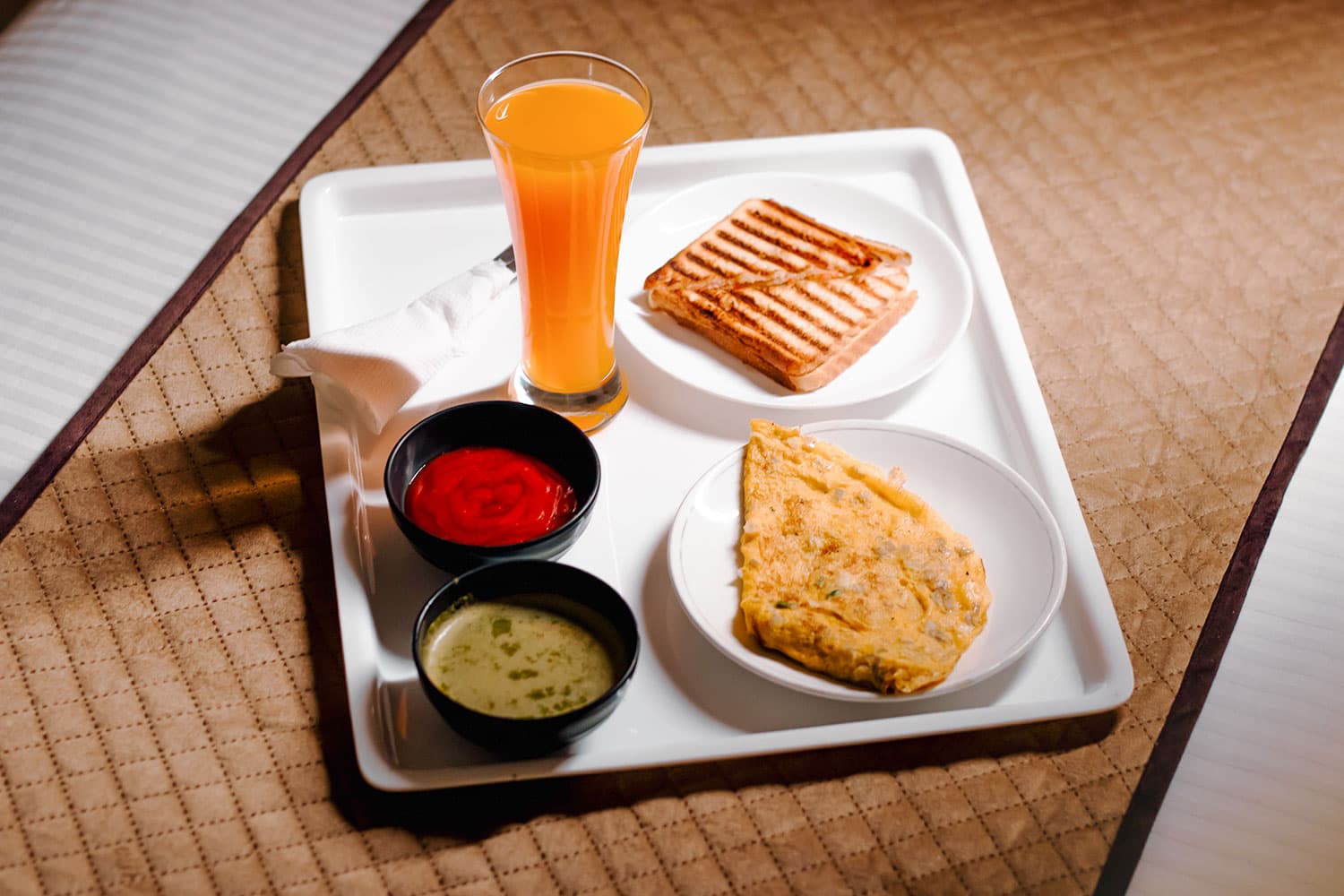 Breakfast tray from above: juice, toast, omelette, ketchup and chutney